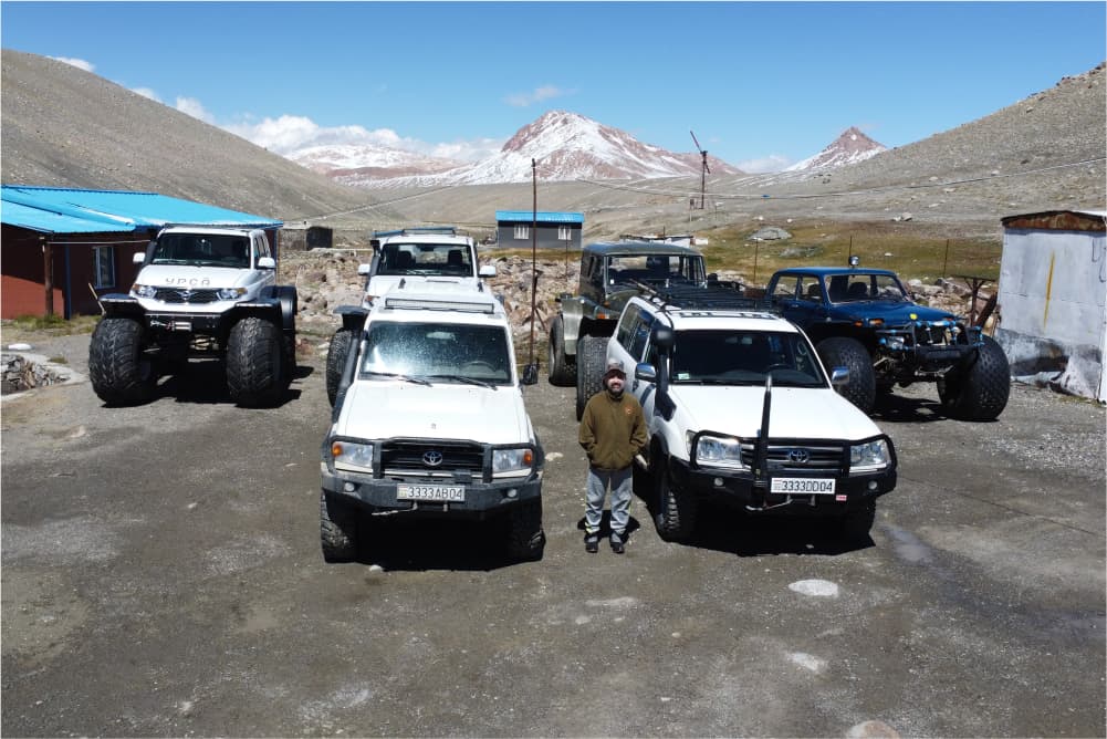 Expedition vehicles parked at camp with Pamir mountains behind them